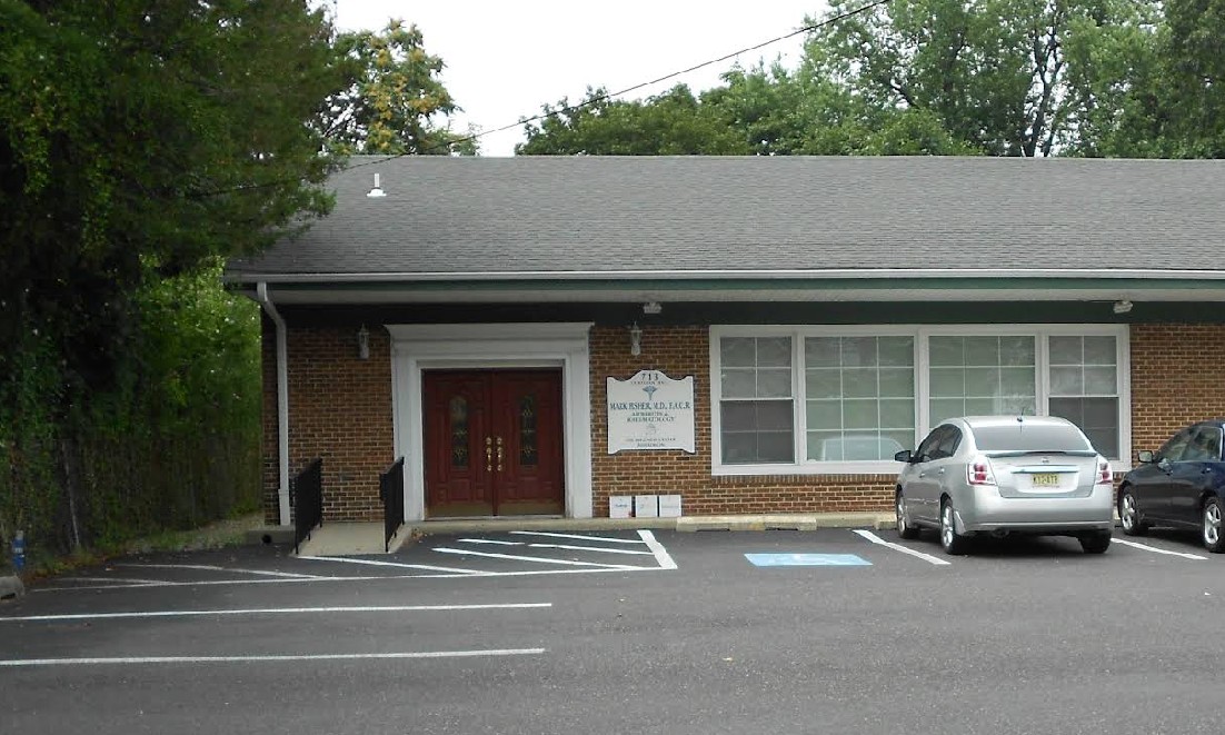 A brick building with a sloped roof, featuring a sign and two parked cars in a lot.