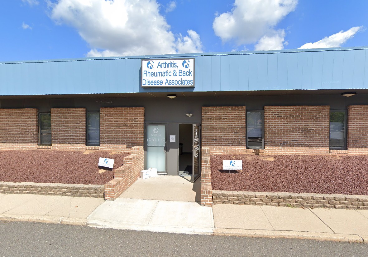 Exterior view of a medical building, 'Arthritis, Rheumatic & Back Disease Associates,' with a blue roof and brick walls.
