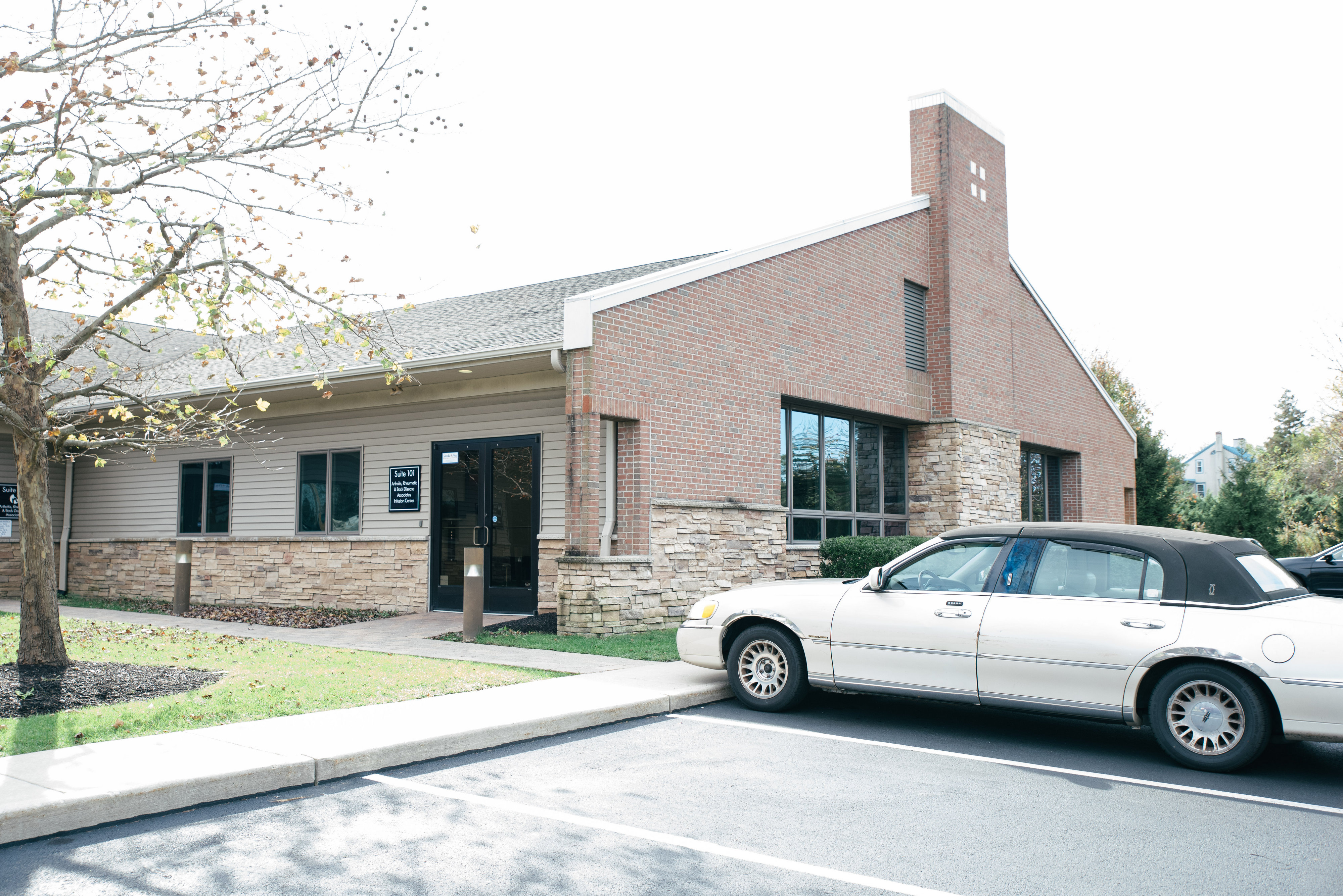 A brick building with large windows, surrounded by a grassy area and several parked cars under a clear sky.