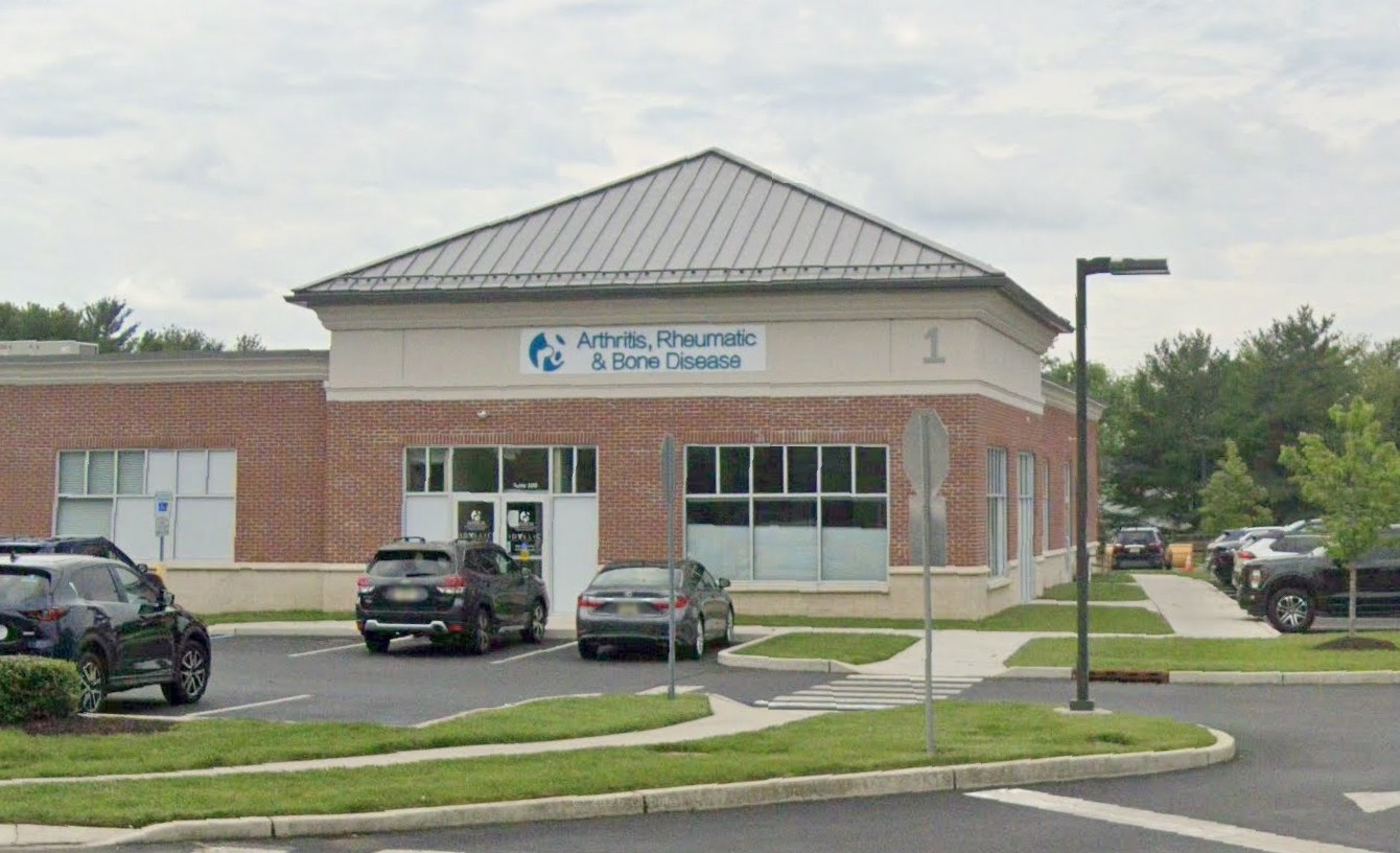 A building with a sign reading 'Arthritis, Rheumatic & Bone Disease' outside, surrounded by parked cars.